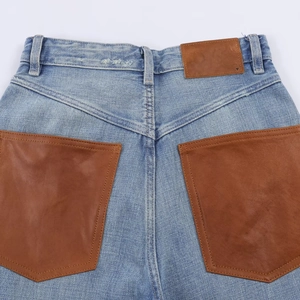 Detail der hellblauen High-Waist-Jeans mit braunen Ledertaschen und Kontrastnähten