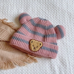 Détail d'un bonnet tricoté rayé rose et gris pour bébé avec écusson ours et oreilles