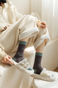 Detail of dark grey crew socks with green trim and bow pattern with plush slippers