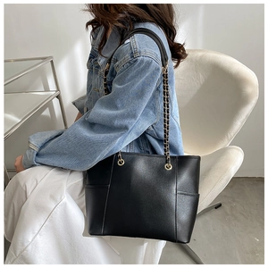 Detail of black leather tote bag with elegant gold chain shoulder strap and matte finish