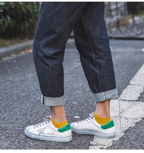 Close-up of white leather sneakers featuring a grey star and green heel tab with jeans