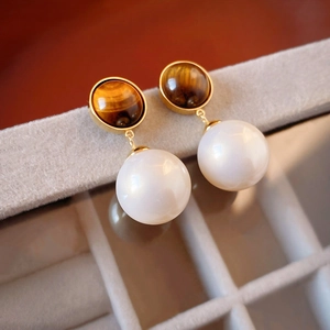 Macro shot of gold-plated earrings with brown tiger eye stone and white pearl beads