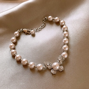 Dettaglio di elegante bracciale di perle a farfalla con micro-pave su raso dorato