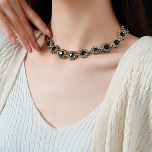 Détail d'un collier vintage doré avec fleurs en cristal bleu porté par un mannequin