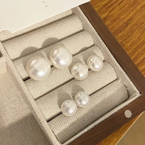 Detailed close-up of three sizes of white round pearl studs in a wooden jewelry box