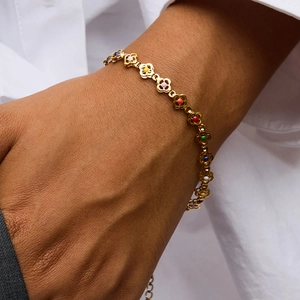 Detail of a gold clover leaf bracelet with colorful enamel links on a model's wrist