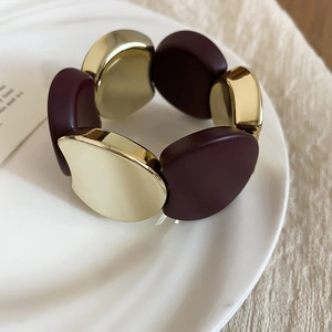 Close-up of gold and deep red acrylic chunky stretch bracelet on a ceramic tray
