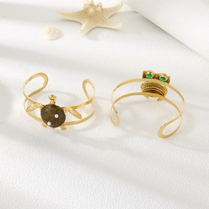 Detailed close-up of gold owl and sea turtle open bangles with pearls and green gems
