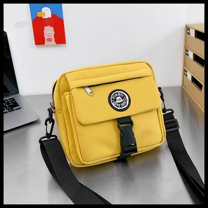 Detail of yellow canvas crossbody bag featuring adjustable black strap and logo badge