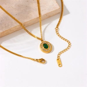 Detail of gold Cuban chain necklace with green stone pendant on a stone display