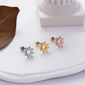 Detailed macro view of gold and silver flower zircon cartilage earrings on stone