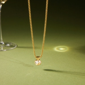 Elegante collana in titanio dorato con ciondolo in zircone cubico su sfondo oliva