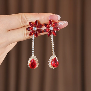 Detailed view of long gold tassel earrings with red floral and teardrop-shaped gemstones