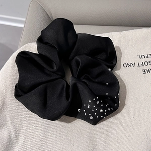 Detailed view of a black satin hair scrunchie with sparkling rhinestones on fabric