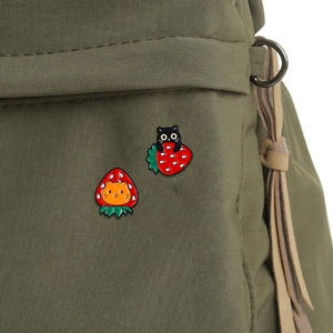 Cute enamel pins featuring black and ginger cats inside strawberries on a green backpack