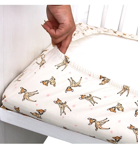 Close-up of elastic edges on a white cotton crib sheet featuring cartoon deer prints