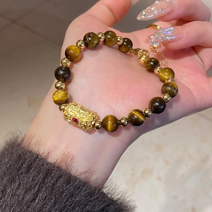 Detail of tiger eye bead bracelet featuring a gold hollow bead with a red gemstone inlay