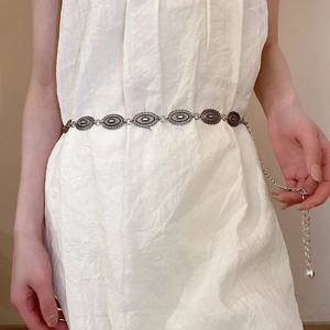 Detailed view of silver metal waist chain with oval engraved charms on a female model