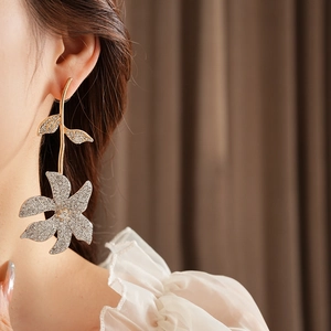 Close-up of elegant gold leaf and silver rhinestone flower earrings worn by a model