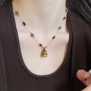 Close-up of a tiger eye gourd pendant necklace worn on a vintage brown knit sweater