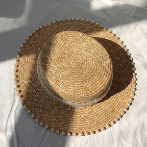 Top view of flat top straw boater hat with pearl accents on white textured fabric