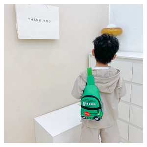 Toddler wearing a bright green school bus cartoon chest bag in a minimalist setting
