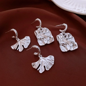 Macro detail of silver ginkgo leaf earrings with irregular textures on silk fabric