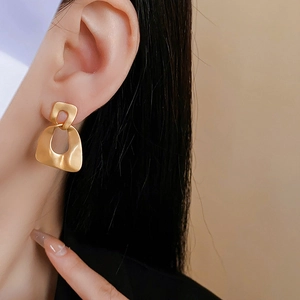 Close-up of matte gold geometric interlocking earrings on model showing metal texture