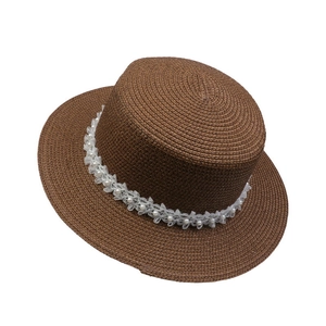 Detail view of brown woven straw hat with white lace ribbon and pearl embellishments