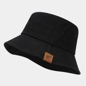 Dettaglio del cappello a secchiello nero con toppa in pelle marrone e cuciture rifinite