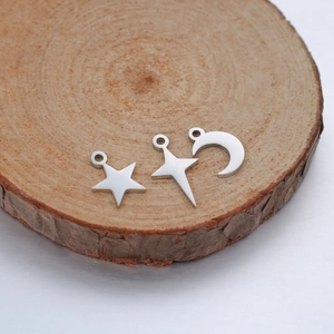 Close-up of polished stainless steel moon and star charms on a natural wood surface