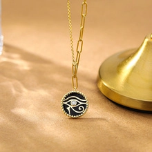 Detail of gold paperclip chain necklace with Eye of Horus black pendant on sand texture