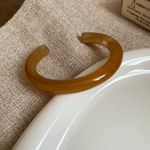 Detail of caramel resin open bangle with marble texture on linen and ceramic dish