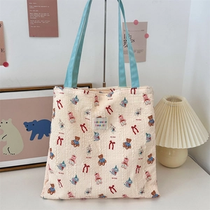 Detail of cream canvas tote bag featuring cute cartoon animal patterns and blue straps