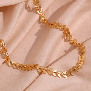 Detailed macro shot of a gold leaf necklace on a champagne silk fabric background