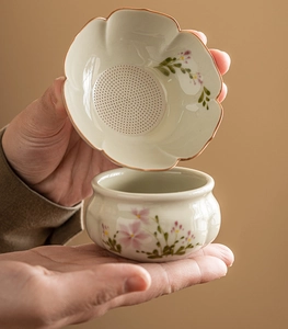 Detail of hand-painted ceramic tea strainer with floral pattern and matching teacup