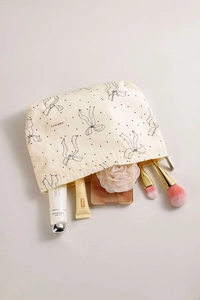 Close-up of cream makeup bag with black bows containing skincare and brushes