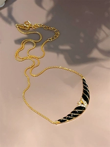 Macro shot of 18K gold necklace with black enamel crescent pendant and white rhinestones