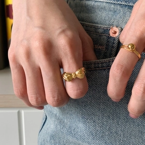 Detailed view of a golden bow ring and bead ring worn by a model on a denim background
