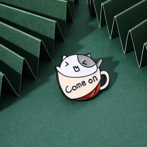 Detail of cartoon cat in a cup enamel pin with Come on text on a green background