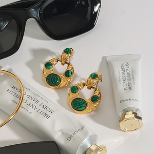 Elegant gold titanium earrings with green malachite stones in a lifestyle setting