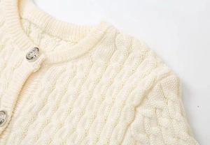 Detailed macro view of cable knit texture and embossed silver buttons on cream cardigan
