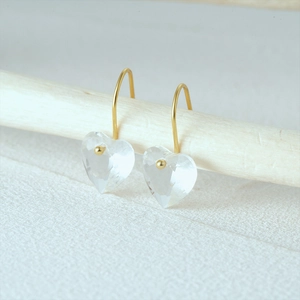 Detail of S925 silver heart crystal drop earrings hanging on a minimal wooden bar
