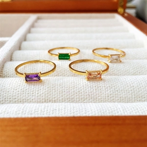 Close-up of four gold rings with purple, green, and clear crystals in a wooden jewelry box