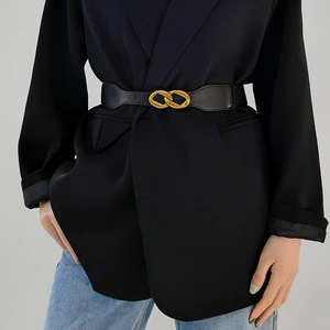 Detail of a black leather waist belt with interlocking gold buckle on a black blazer suit