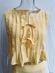 Detail of light yellow pleated sleeveless top with bow tie closures and textured fabric
