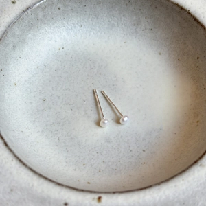 Détail de boucles d'oreilles perles en argent S925 minimalistes sur une plaque en céramique
