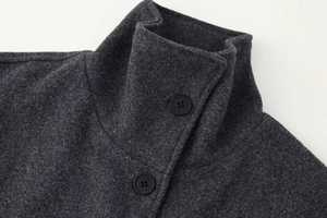 Detail view of the mock neck and black buttons on a dark grey wool coat with fabric texture