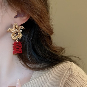 Gros plan sur des boucles d'oreilles fleurs dorées avec pompon rouge Double Bonheur