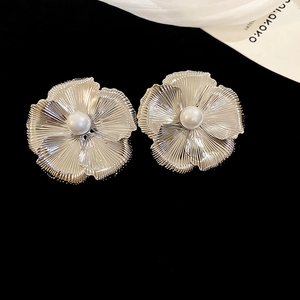 Macro shot of metallic flower earrings with brushed texture and central white pearl